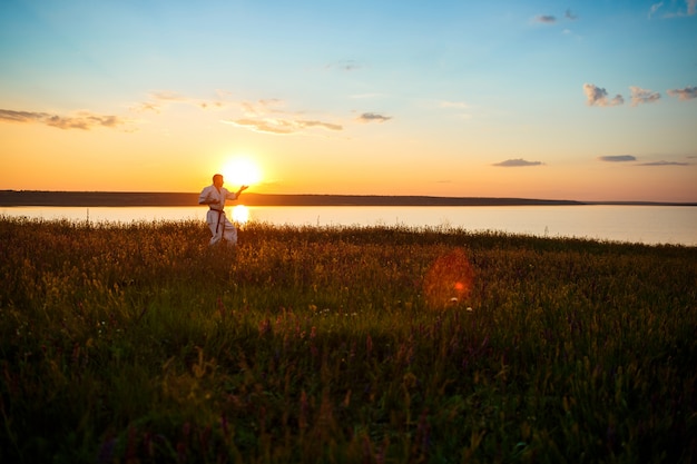 Free photo silhouette of sportive man training karate in field at sunrise.