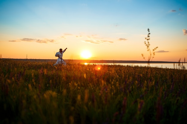 Free photo silhouette of sportive man training karate in field at sunrise.