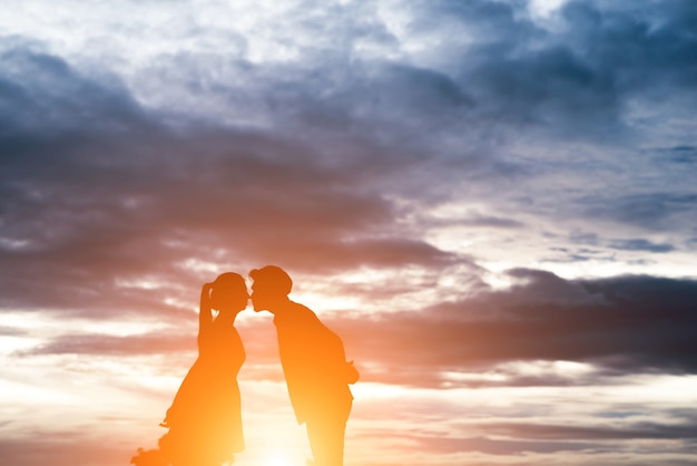 Silhouette of sweet couple kissing over sunset background.