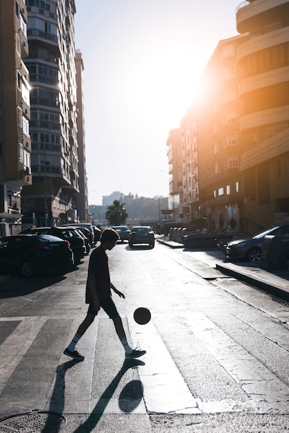 Free photo silhouette of a teenage boy playing basketball on street in city