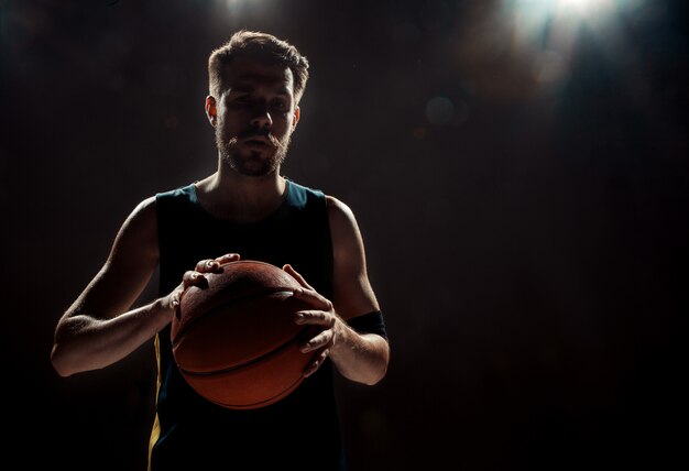 Silhouette view of a basketball player holding basket ball on black wall