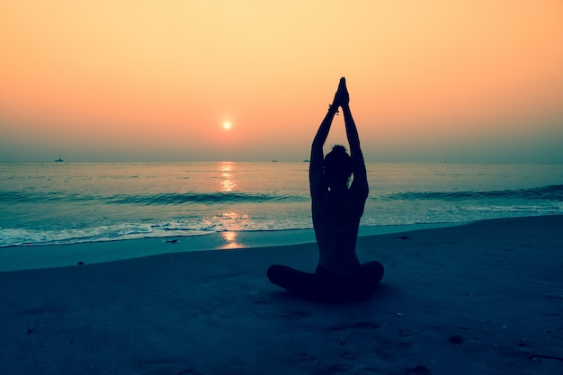 Silhouette of woman doing yoga on a beach