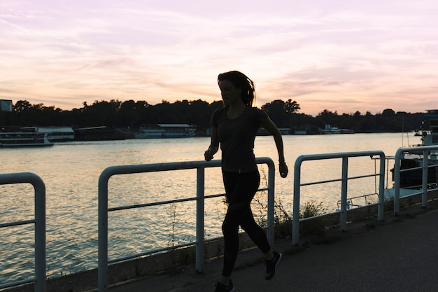 Free photo silhouette of a woman running on street near river