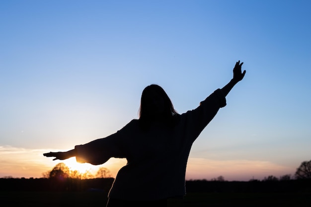 Silhouette of a woman at sunset in a field against the sky rear view