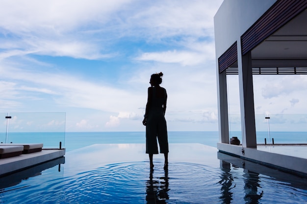 Free photo silhouette of a woman walking on the water surface of the infinity pool of an expensive rich luxury villa on a mountain with a sea view