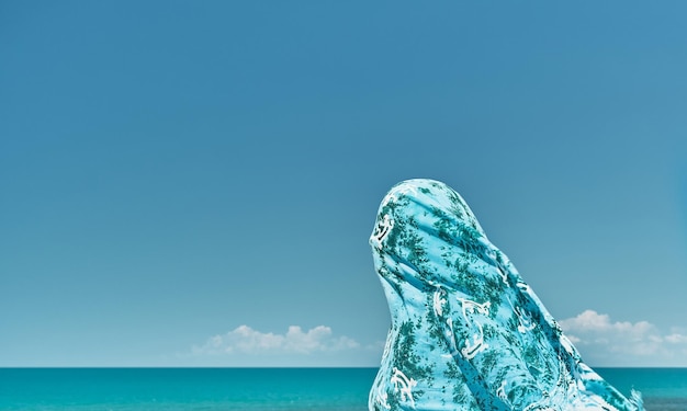 Silhouette of a woman wrapped in a scarf against a gust of wind against the background of the summer sea and blue clear sky weekend at sea cool breeze