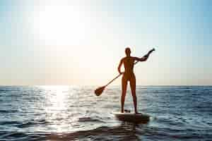 Free photo silhouette of young beautiful woman surfing in sea at sunrise.