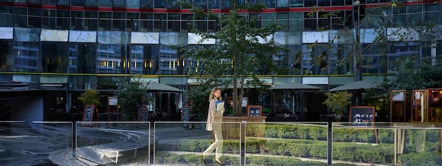 Free photo silhouette of young business woman in beige suit walking in city center posing near office buildings