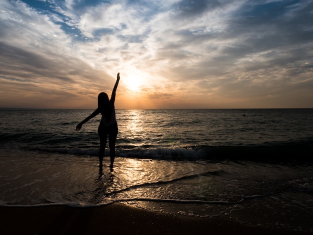 Free photo silhouette of a young girl on the beach. young girl is walking at sunset by the sea.tourist girl on beach holiday.