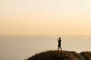 Free photo silhouette of a young man taking pictures of the sea on a smartphone during sunset. evening, summer travel on vacation