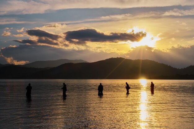 Silhouettes of fishermen against the background of the setting sun clouds and silhouettes of mountains selective focus idea for a background or wallpaper beautiful natural landscape