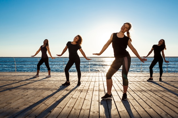 Free photo silhouettes of sportive women dancing zumba near sea at sunrise