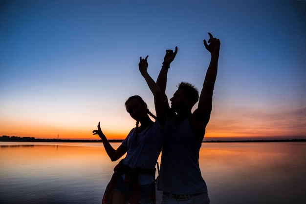 Silhouettes of young beautiful couple resting rejoicing at sunrise near lake