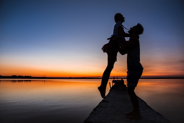 Free photo silhouettes of young beautiful couple resting rejoicing at sunrise near lake