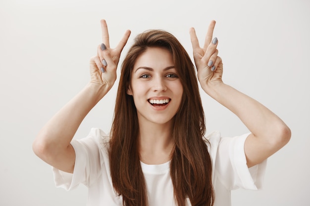 Free photo silly adorable girl showing quotation marks gesture and smiling happy