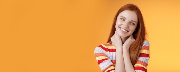 Silly enthusiastic attractive redhead blueeyed girl tilting head touching neck flirty smiling enjoy perfect day feel happiness joy giggling coquettish flirting boyfriend standing orange background