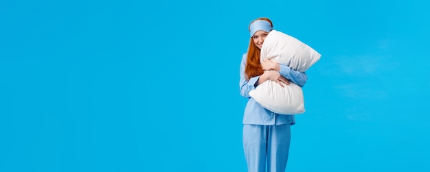 Free Photo silly romantic and cute gentle young redhead coquettish woman in pyjama and sleep mask hugging pillo