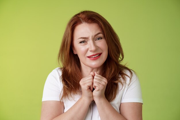 Silly touched tender redhead charmed middleaged woman sighing gladly gaze admiration delighted press hands together heartwarmed fascinated look grateful lovely camera green wall