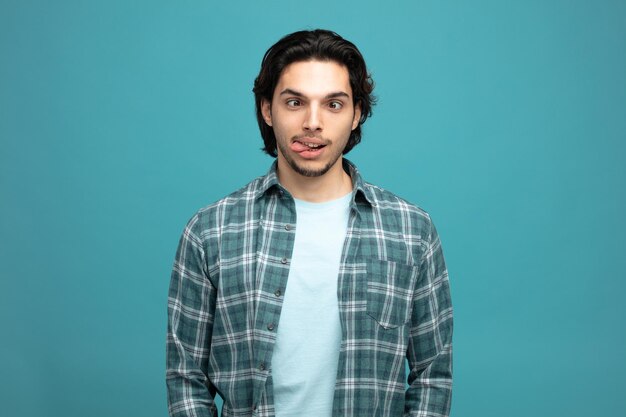 silly young handsome man crossing eyes and showing tongue isolated on blue background