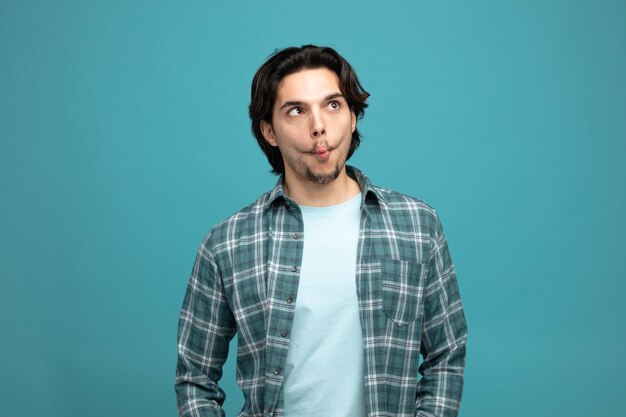 silly young handsome man looking at side making fish gesture with crossed eyes isolated on blue background