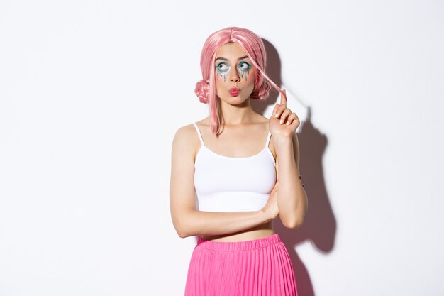 Silly young party girl in pink wig and halloween makeup, looking at upper left corner thoughtful, standing coquettish.