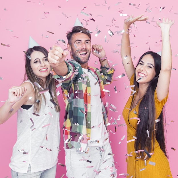 Silver confetti falling over the friends dancing against pink background