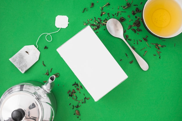 Silver teapot, spoon and herbal tea on green background