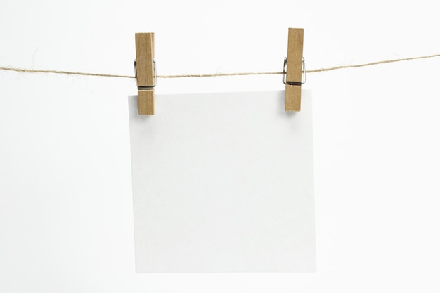 Free Photo single empty paper sheet for notes that hang on a rope with clothespins and isolated on white.