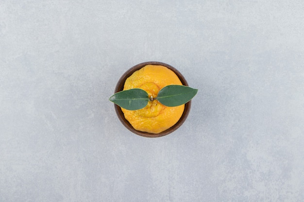 Free photo single fresh tangerine with leaves in wooden bowl.