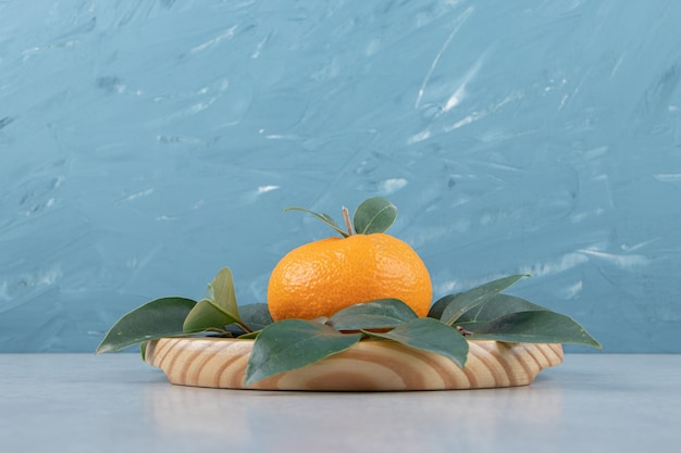 Single fresh tangerine with leaves on wooden plate. 