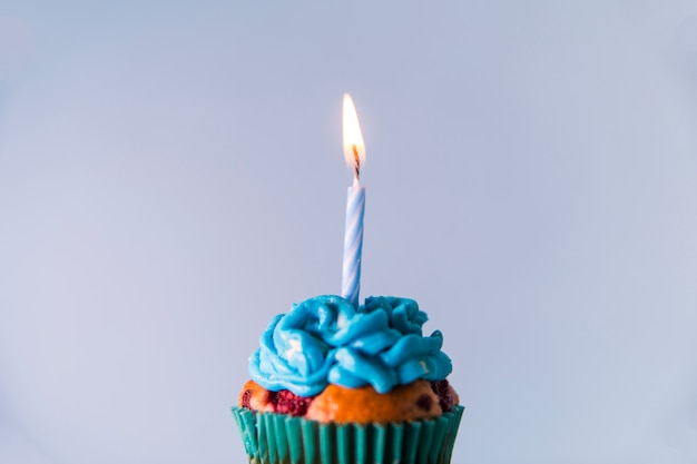 Free photo single lighted candle over the cupcake against blue backdrop