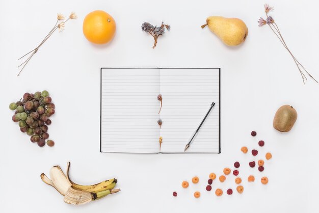 Single line notebook with notebook; pen; croissant; fruits; coffee and dried flowers on white backdrop