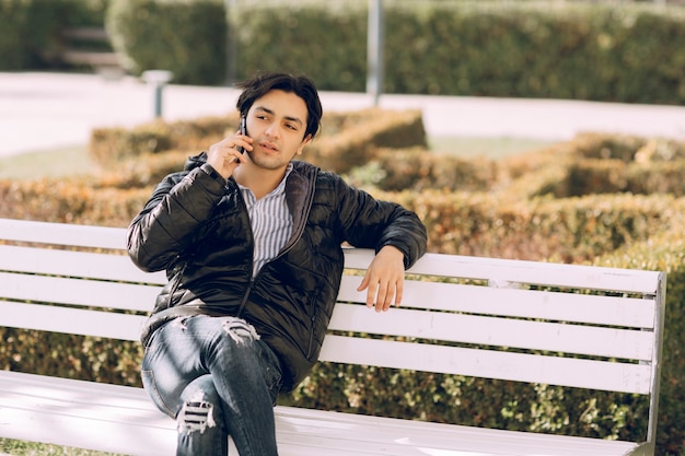 Single man sitting on the bench in the park and talking to the phone. High quality photo