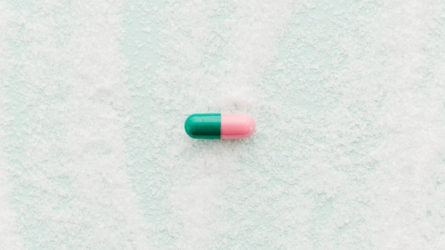 Free photo single pink and green capsules on salt background