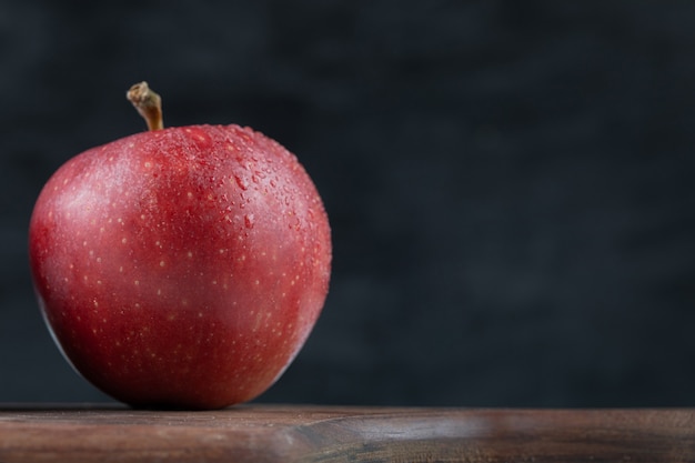 A single red apple on a wooden platter