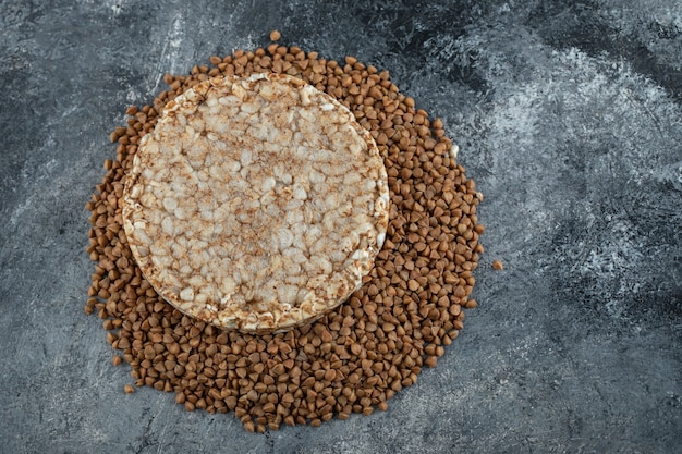 Single rice cake and uncooked buckwheat on marble surface