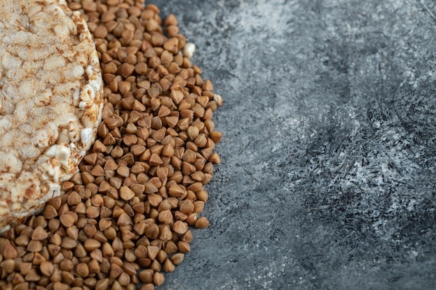 Single rice cake and uncooked buckwheat on marble surface