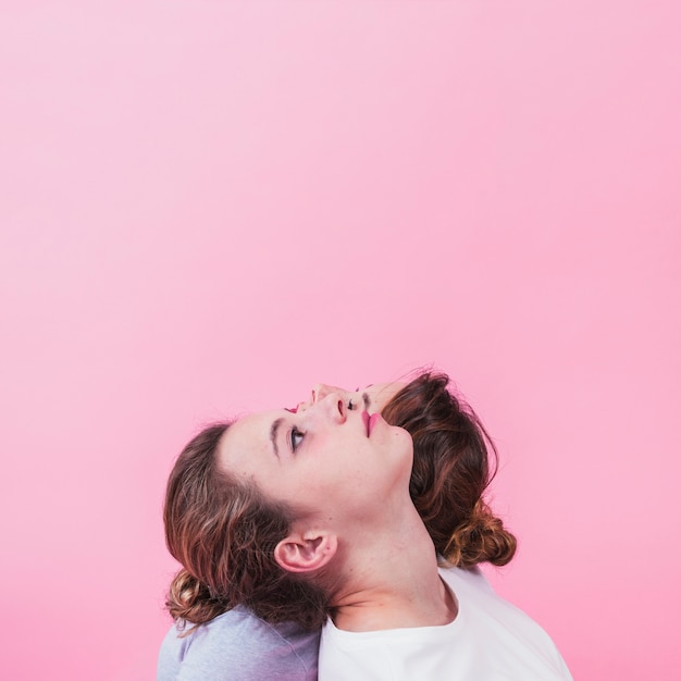 Free photo sister's leaning head on each other's shoulder against pink background