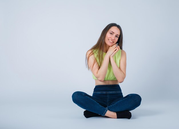 Sitting on floor girl is looking at camera by holdin hands on chest on white background