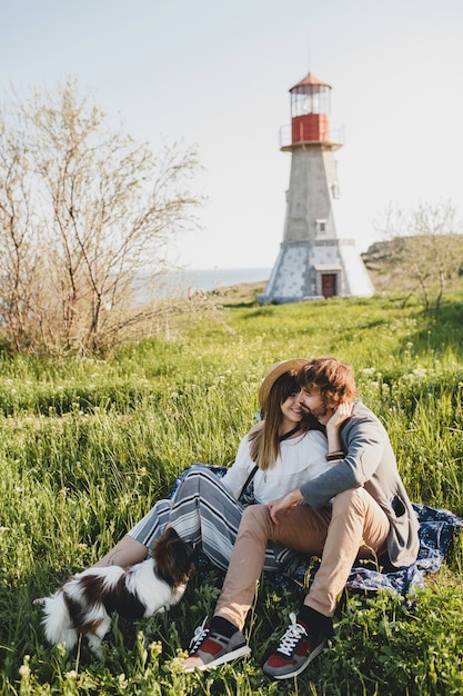 Sitting in grass young stylish hipster couple in love walking with dog in countryside