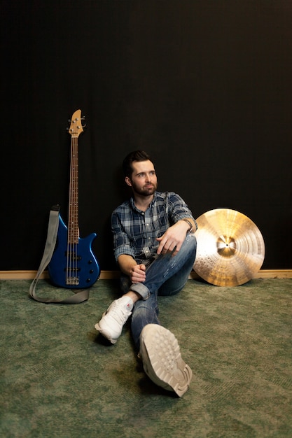 Free photo sitting guitarist leaning against wall