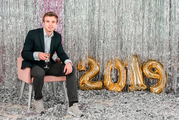 Free photo sitting man next to golden balloons new year party