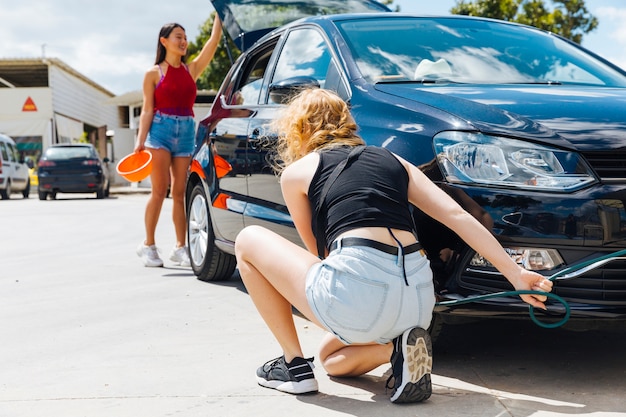 Free photo sitting woman inflating tire while other female opening trunk