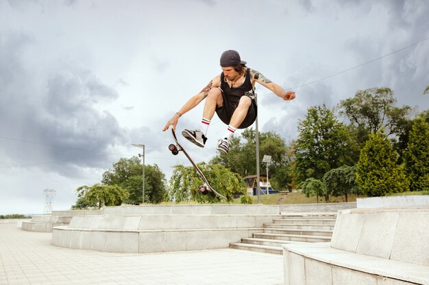 Skateboarder doing a trick at the city's street in cloudly day. Young man in sneakers and cap riding and longboarding on the asphalt. Concept of leisure activity, sport, extreme, hobby and motion.