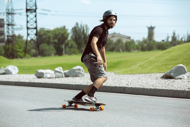 Skateboarder doing a trick at the city's street in sunny day. Young man in equipment riding and longboarding on the asphalt in action. Concept of leisure activity, sport, extreme, hobby and motion.