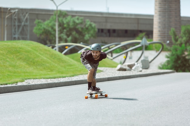 Skateboarder doing a trick at the city's street in sunny day. Young man in equipment riding and longboarding on the asphalt in action. Concept of leisure activity, sport, extreme, hobby and motion.