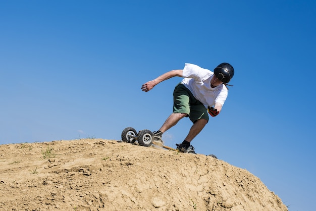 Skateboarder jumping with mountainboard over the hill with blue sky