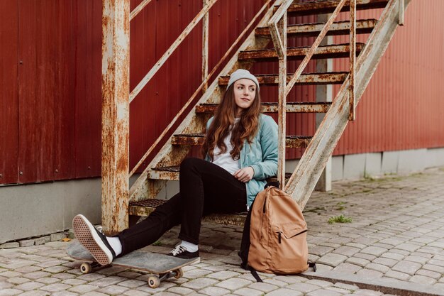 Skater girl in the urban sitting on stairs long view