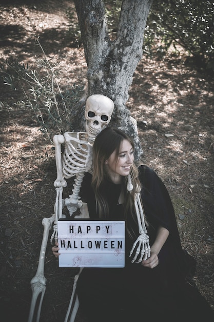 Free Photo skeleton hugging smiling lady with tablet in dark clothes