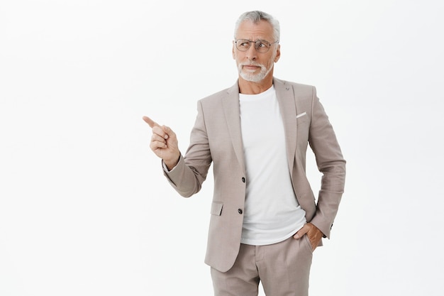 Skeptical businessman in suit and glasses pointing finger left thoughtful